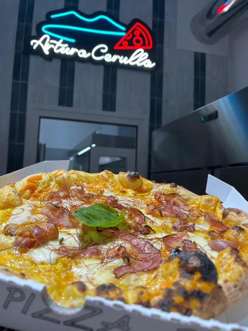 Pizza zucca e pancetta sotto l'insegna neon della pizzeria